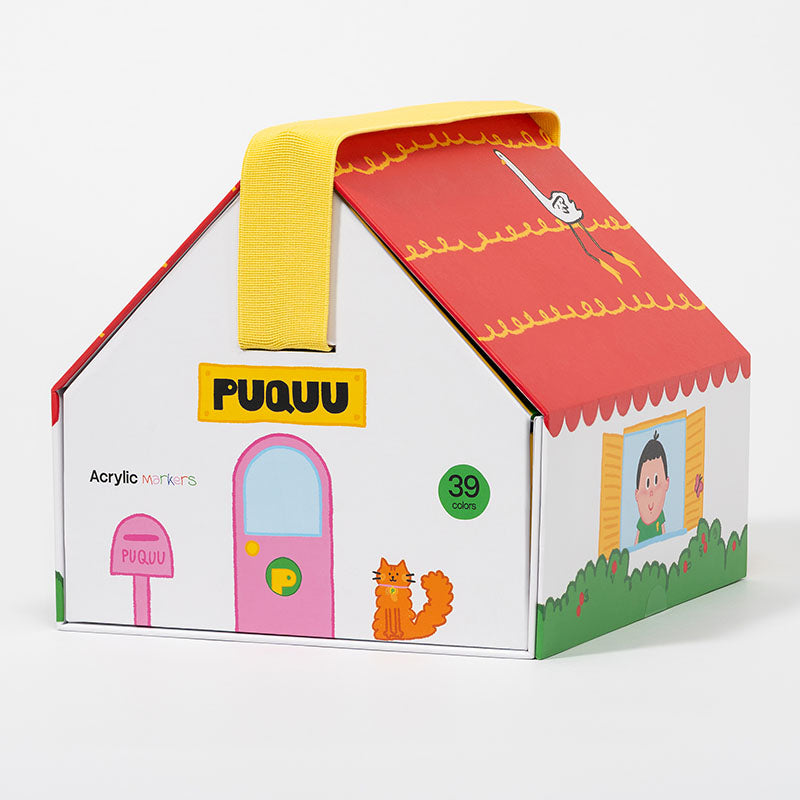 A house-shaped PUQUU acrylic markers box with a yellow handle, featuring colorful illustrations of a pink door, red roof, green grass, and a cat on a white background.