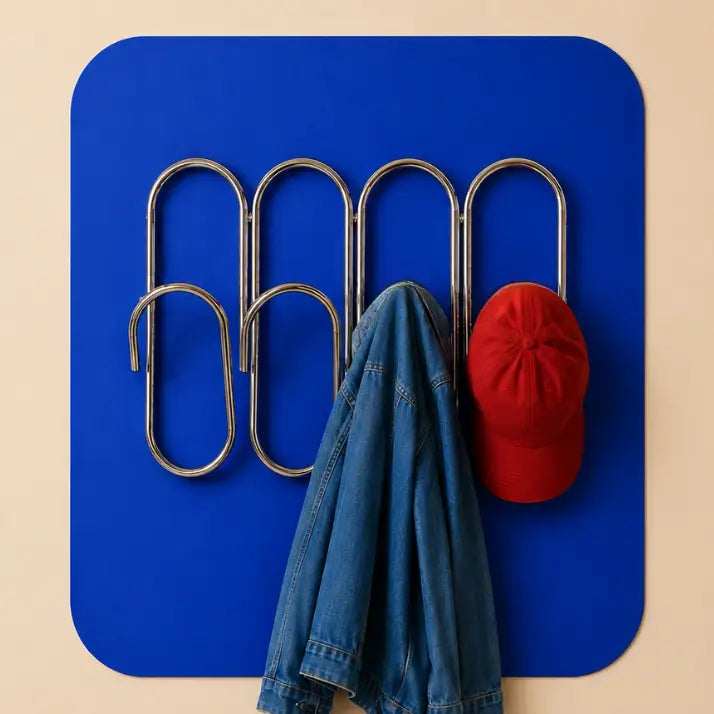paperclip style coat rack with denim jacket and red baseball cap hanging on a wall with blue background.