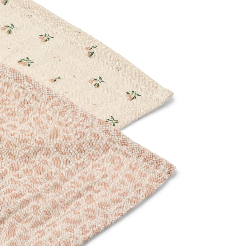 A close-up of a folded muslin baby cloth showing two sides: one side has a light peach-beige leopard print, and the other side is cream with small embroidered peach flowers and green leaves.