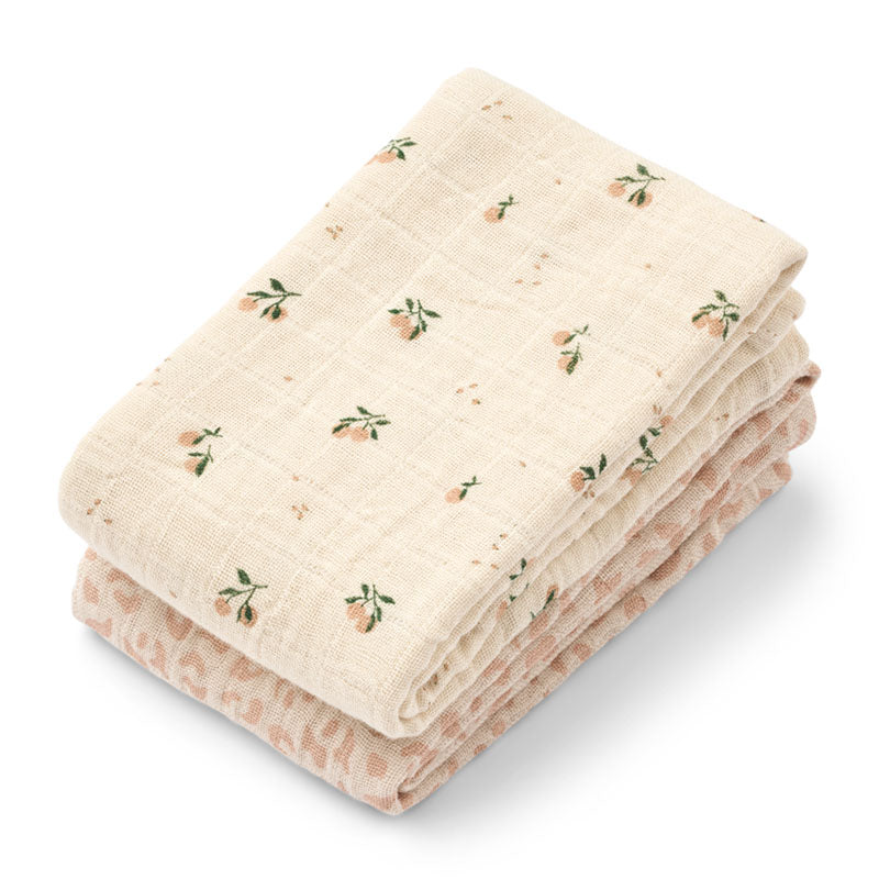 Two folded muslin baby muslin cloths. The top cloth is cream with a small peach and green floral pattern, and the bottom blanket is a soft dusty pink with a subtle leopard print.