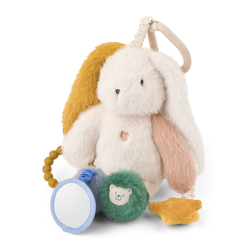 A plush baby sensory toy shaped like a white bunny with long floppy ears in cream, blush pink, and mustard yellow. The toy includes a beige hanging loop, a small heart-shaped charm, a blue-and-white circular mirror, a green plush pom-pom with a bear face, and a yellow star.