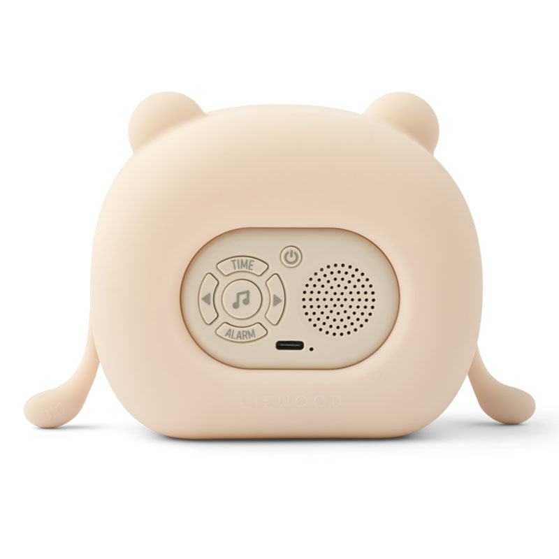 A cute, bear-shaped portable alarm clock in a warm cream-beige color, featuring a rounded body, small ears on top, and small legs on the sides. The back has a central control panel with buttons for time, music, alarm, and power, alongside a speaker grille and a USB-C port.