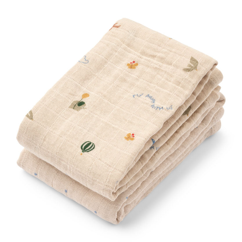 A stack of two folded muslin baby cloths in a warm beige color, decorated with small, scattered embroidered motifs including a hot air balloon, a duck, and a bird.