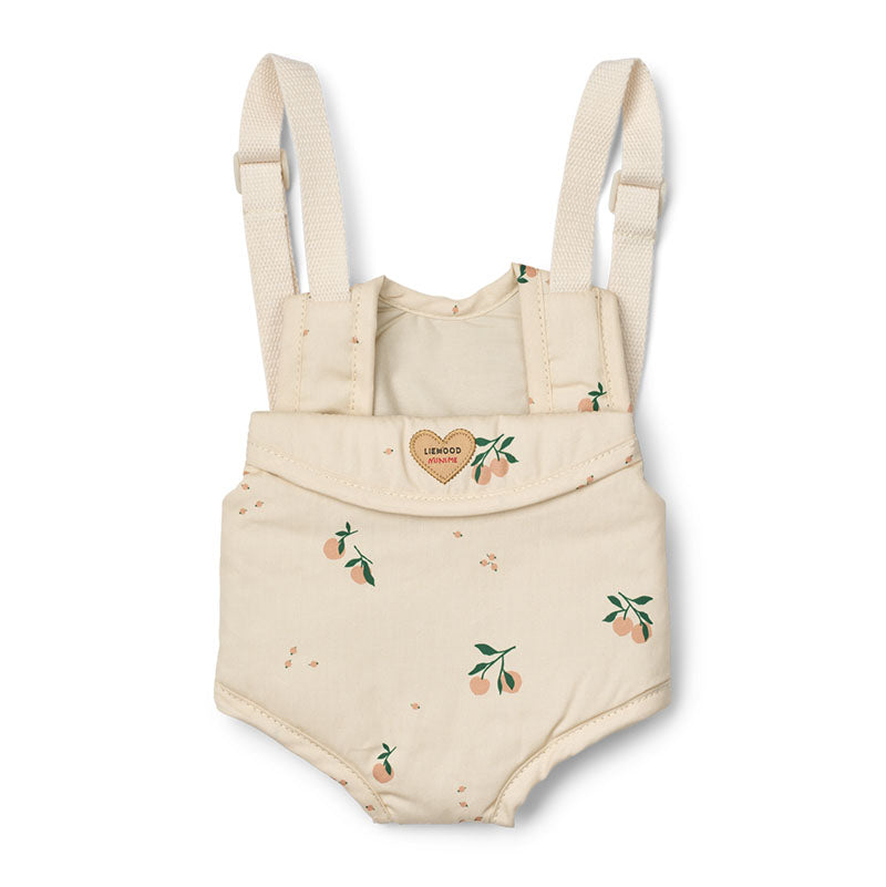A Liewood doll carrier with adjustable shoulder straps, featuring a small peach and green leaf print scattered across the fabric and a small heart-shaped patch on the front flap.