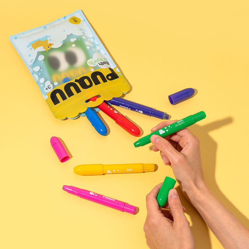 A set of colorful highlighters and a branded pouch on a bright yellow background, with two hands holding a green highlighter and its cap.