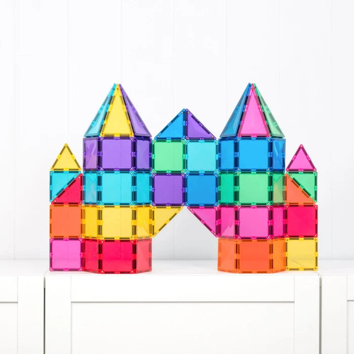 A colorful set of transparent plastic building tiles arranged to form a castle-like structure, displayed on a white surface against a white paneled wall.