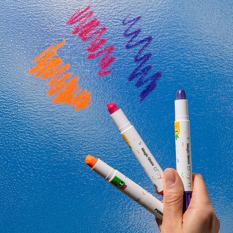 A hand holds three Magic Color GEL markers against a textured blue glass surface, with orange, pink, and purple scribbles drawn above. The markers have white bodies with colorful confetti details and purple, orange, and pink tips.