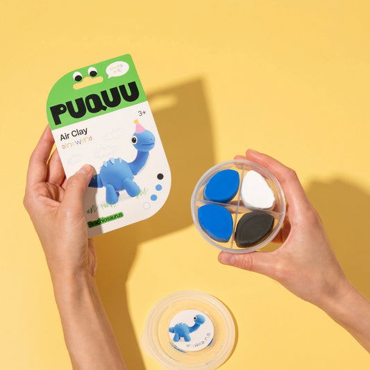 A person holds a package of PUQUUU Air Clay playdough and a round four-compartment tray showing the colored clay pieces. Another tray is shown below with a printed insert.
