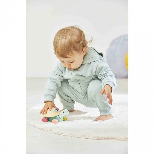Child in a light blue onesie playing with a toy on a white surface.
